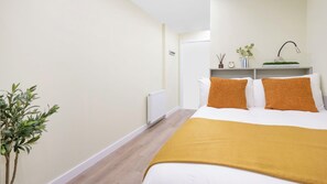 Un dormitorio con una cama, un radiador, un estante con adornos y una planta.
