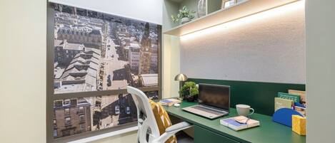 A modern office space with a green desk, a laptop, a cup, and a view of a cityscape through a large window.