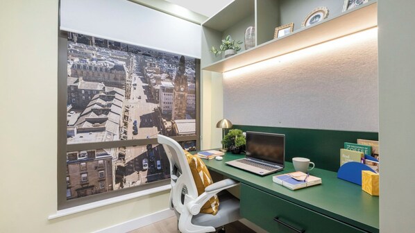 Un espacio de oficina moderno con un escritorio verde, una computadora portátil, una taza y vistas a un paisaje urbano a través de un ventanal grande.