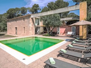 A poolside area with lounge chairs, a swimming pool, and a building with a stone facade. - Viterbo by Interhome (Son Servera)