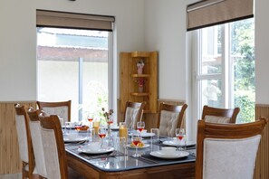 Ein Essbereich mit einem Tisch für sechs Personen, Stühlen, einer Holzkommode und großen Fenstern mit Aussicht.