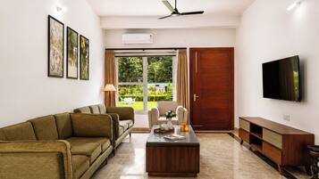 A living room with a sofa, a coffee table, a TV, and a door leading to a garden.