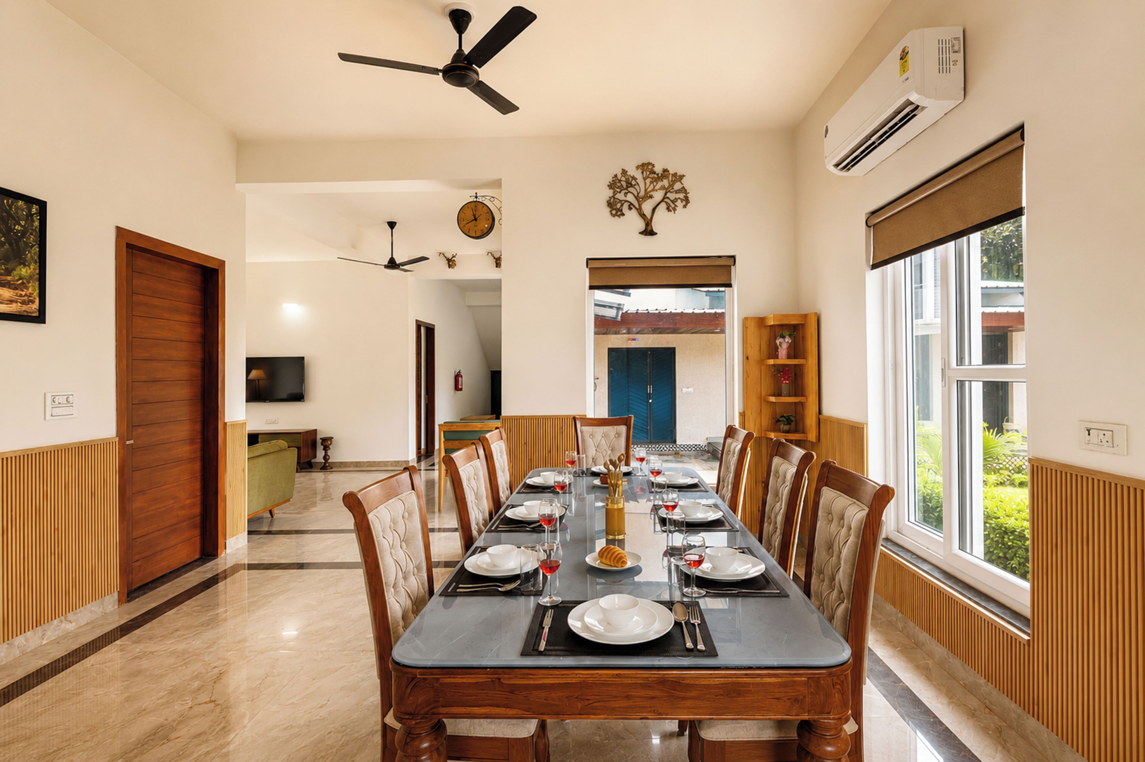 A dining area with a long table set for six, flanked by wooden paneling and a large window.