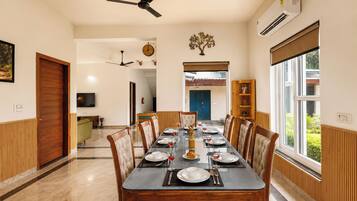 A dining area with a long table set for six, flanked by wooden paneling and a large window.