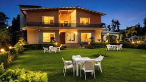 Una casa a due piani con un balcone, un prato con mobili da esterno e un ingresso ben illuminato.