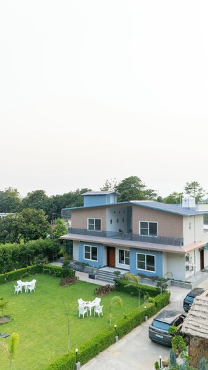 Un edificio de dos pisos con techo plano, un balcón visible y un césped bien cuidado con mobiliario exterior.