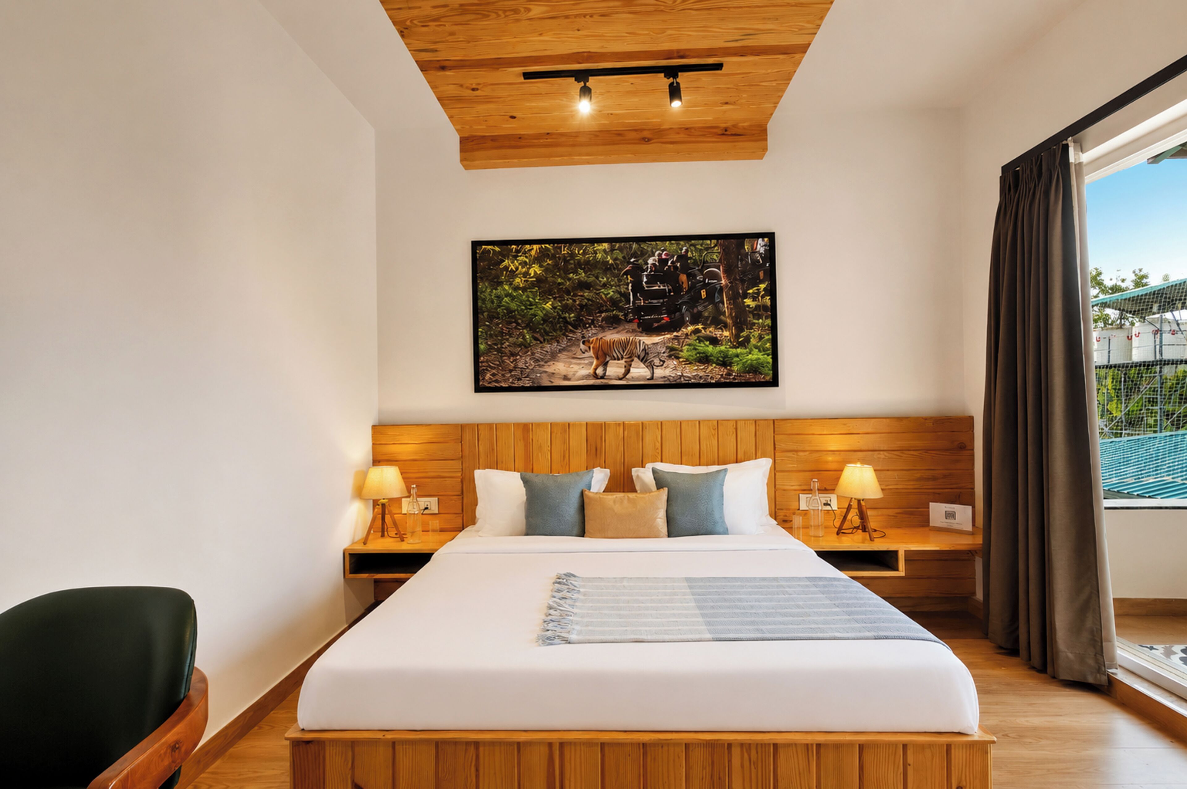Habitación de hotel con techo de madera, una cama grande con ropa blanca, dos mesitas de noche con lámparas y un cuadro en la pared.