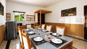 Un'area pranzo con un tavolo lungo apparecchiato per un pasto, una cucina sullo sfondo e vista sul verde attraverso la finestra.