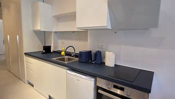 Una cocina moderna con armarios blancos, un refrigerador de acero inoxidable, lavavajillas, horno empotrado y encimera negra.