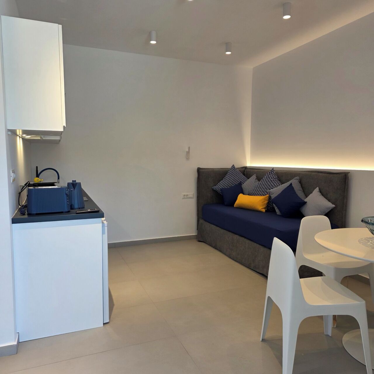A modern room with a sofa, a dining table, and a kitchenette.