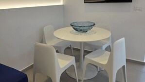 Una zona de dinar moderna amb una taula rodona, cadires blanques i un centre de taula amb bol de vidre. Un televisor de pantalla plana està muntat a la paret sobre la taula.