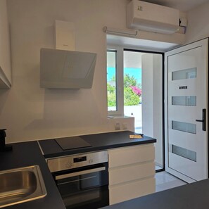 A modern kitchen with a built-in oven, a dishwasher, and a window with a view of greenery.