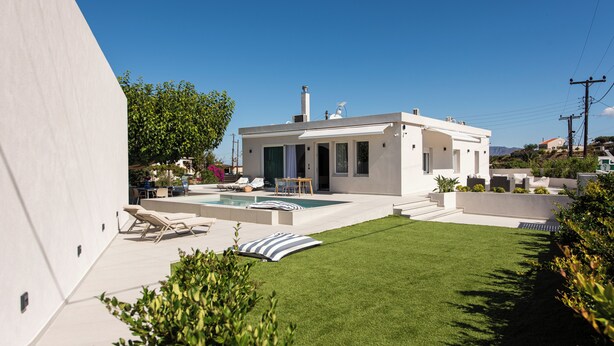 Una casa moderna amb piscina, un patio amb gandules i un jardí ben cuidat.