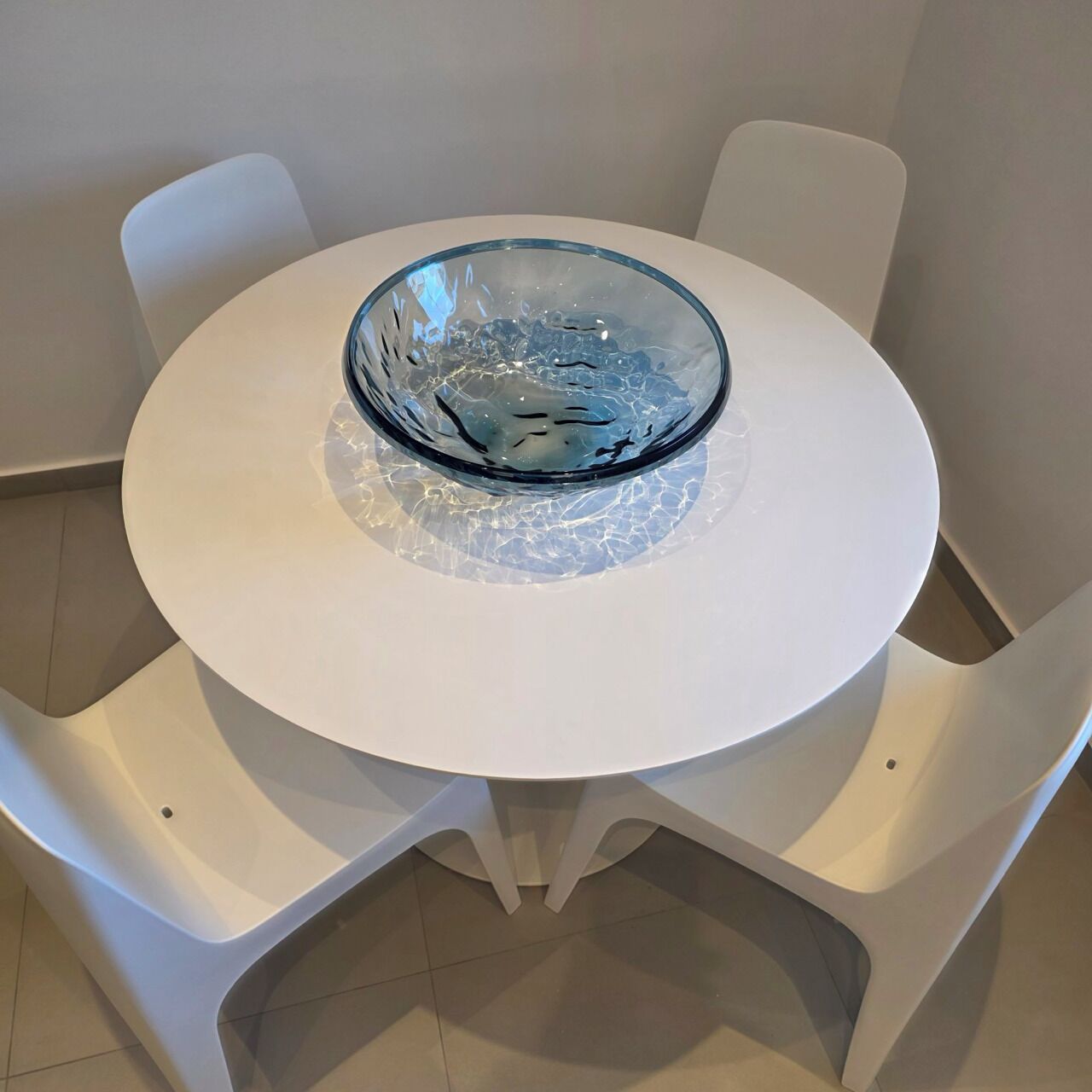 A round white table with a glass bowl on top, surrounded by white chairs.