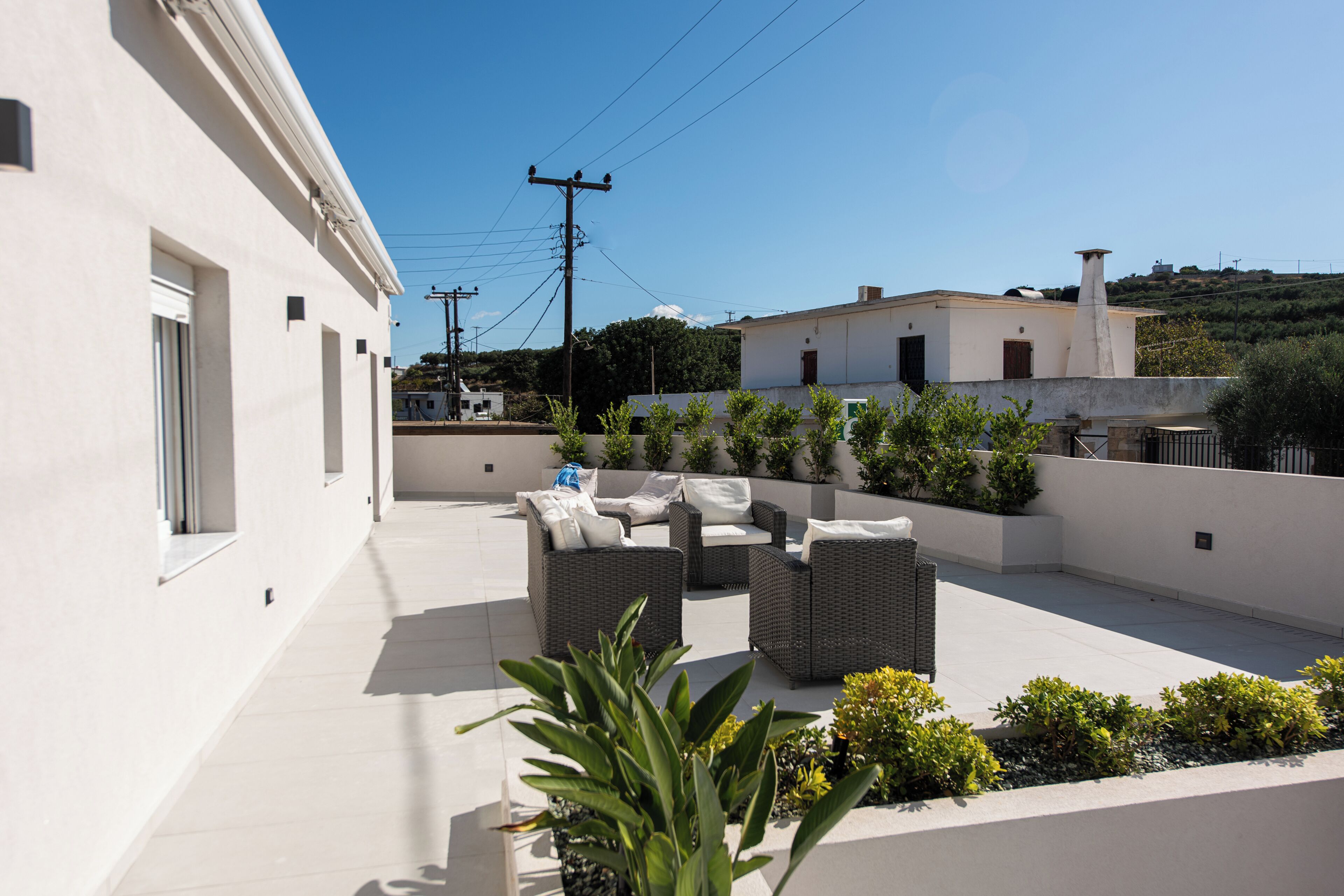 Una terraza en la azotea con mobiliario exterior, un edificio blanco y vistas del entorno.