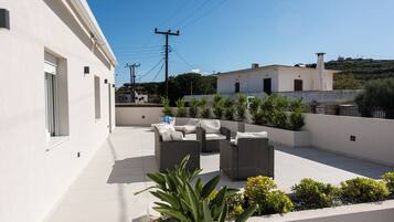 Una terraza en la azotea con mobiliario exterior, un edificio blanco y vistas del entorno.