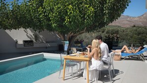 A poolside area with a dining table, chairs, and a lounge chair. - Azure West by Cozy Corner (Ag. Georgios)
