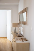 A minimalist room with a wooden dresser, a lamp, a decorative piece, and a mirror on the wall.