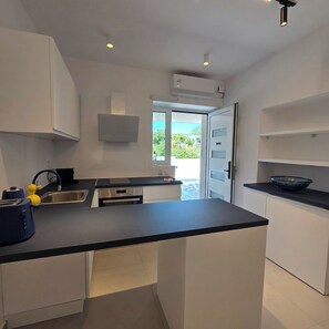 Una cocina moderna con armarios blancos, encimera negra y ventana con vistas a la vegetación.