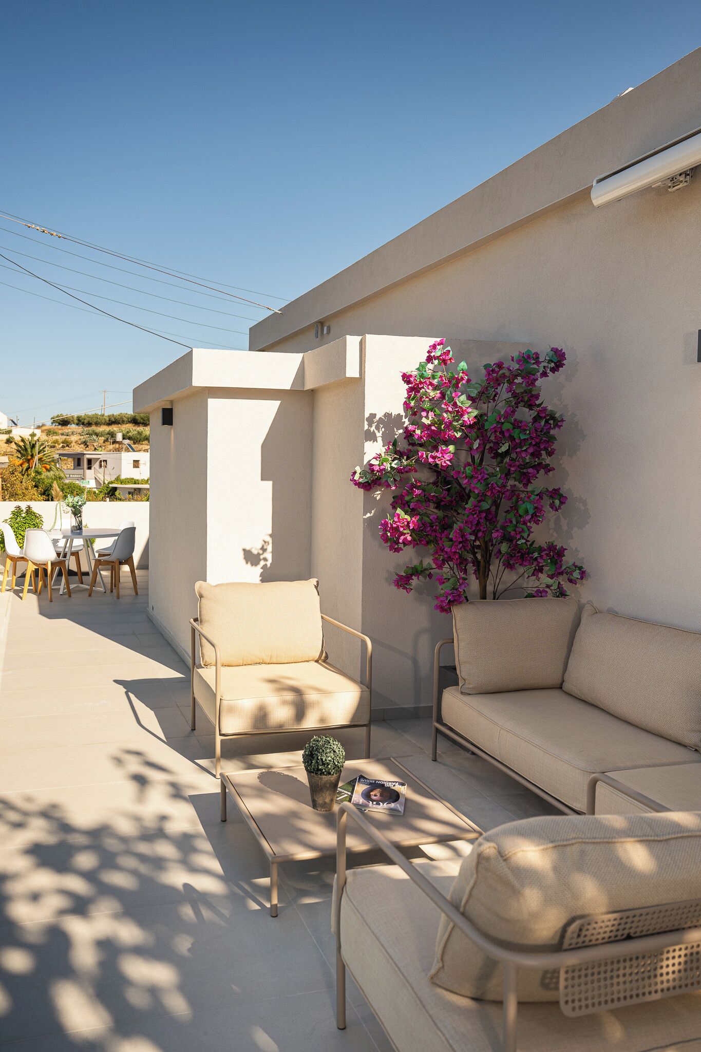 A sunlit outdoor seating area with a sofa and chairs, a small table, and a potted plant.