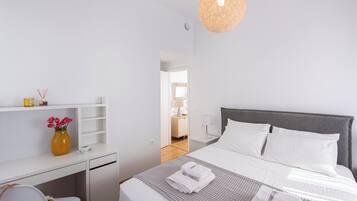 A modern bedroom with a bed, bedside table, and a desk with a vase of flowers.