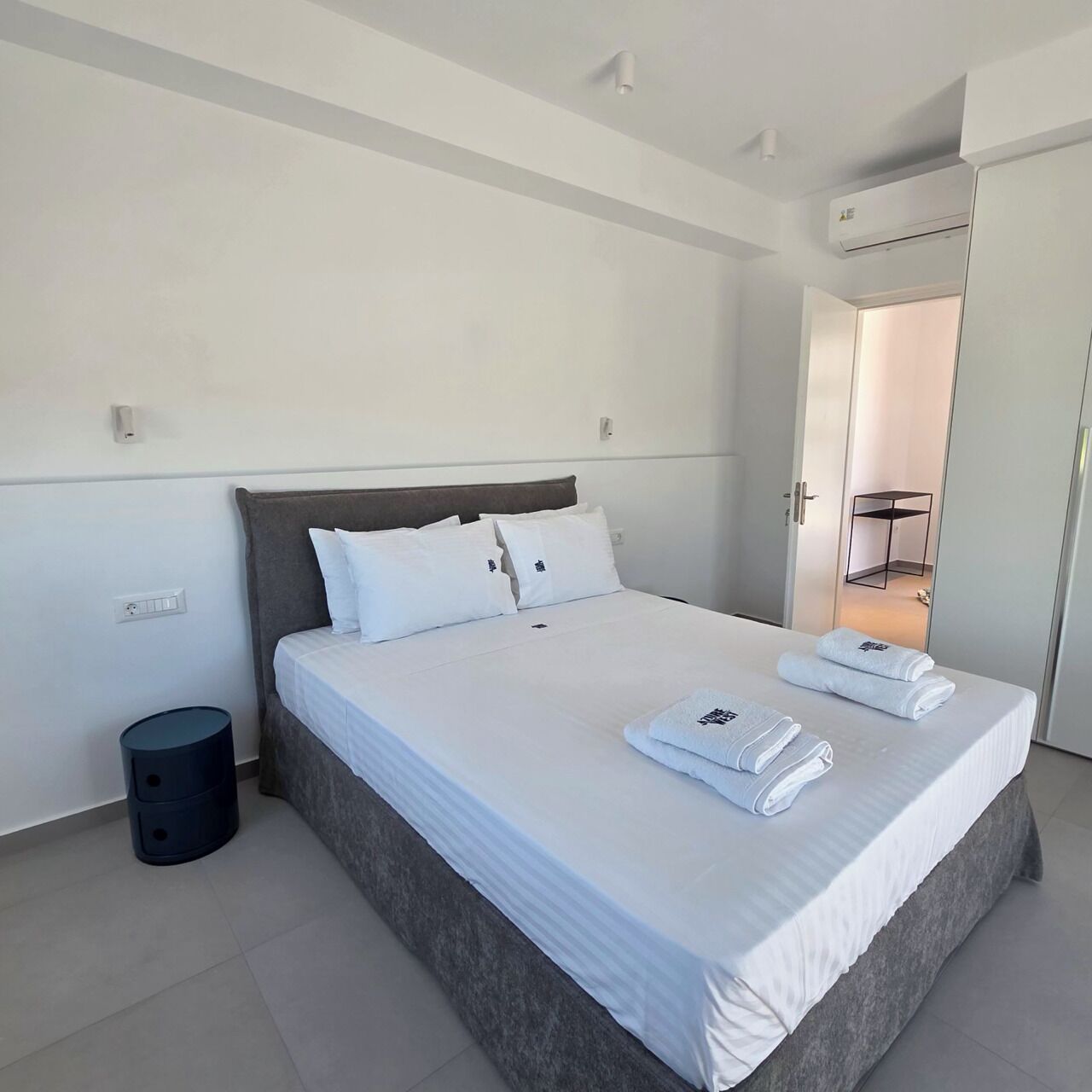 Habitación de hotel moderna con una cama grande, una mesita de noche, un cesto de basura pequeño y un armario con espejo.
