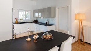 A modern kitchen with white cabinets, a black countertop, and a dining area with a table set for two. - Azure West by Cozy Corner (Ag. Georgios)