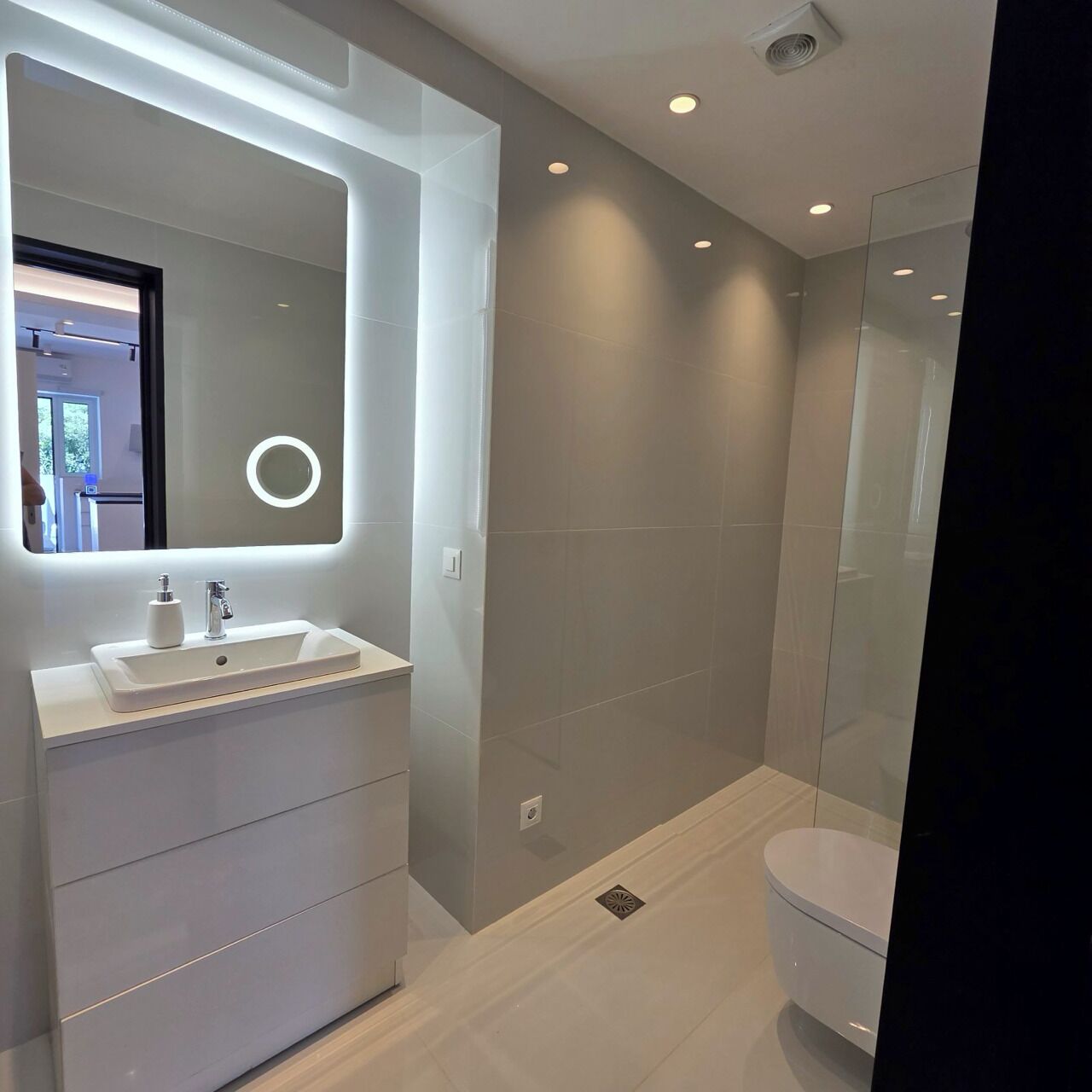 A modern bathroom with a large mirror, a white sink, and a toilet.