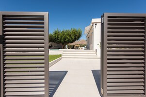 A pathway leading to a building with a modern architectural style, featuring a clear sky and a tree-lined background.