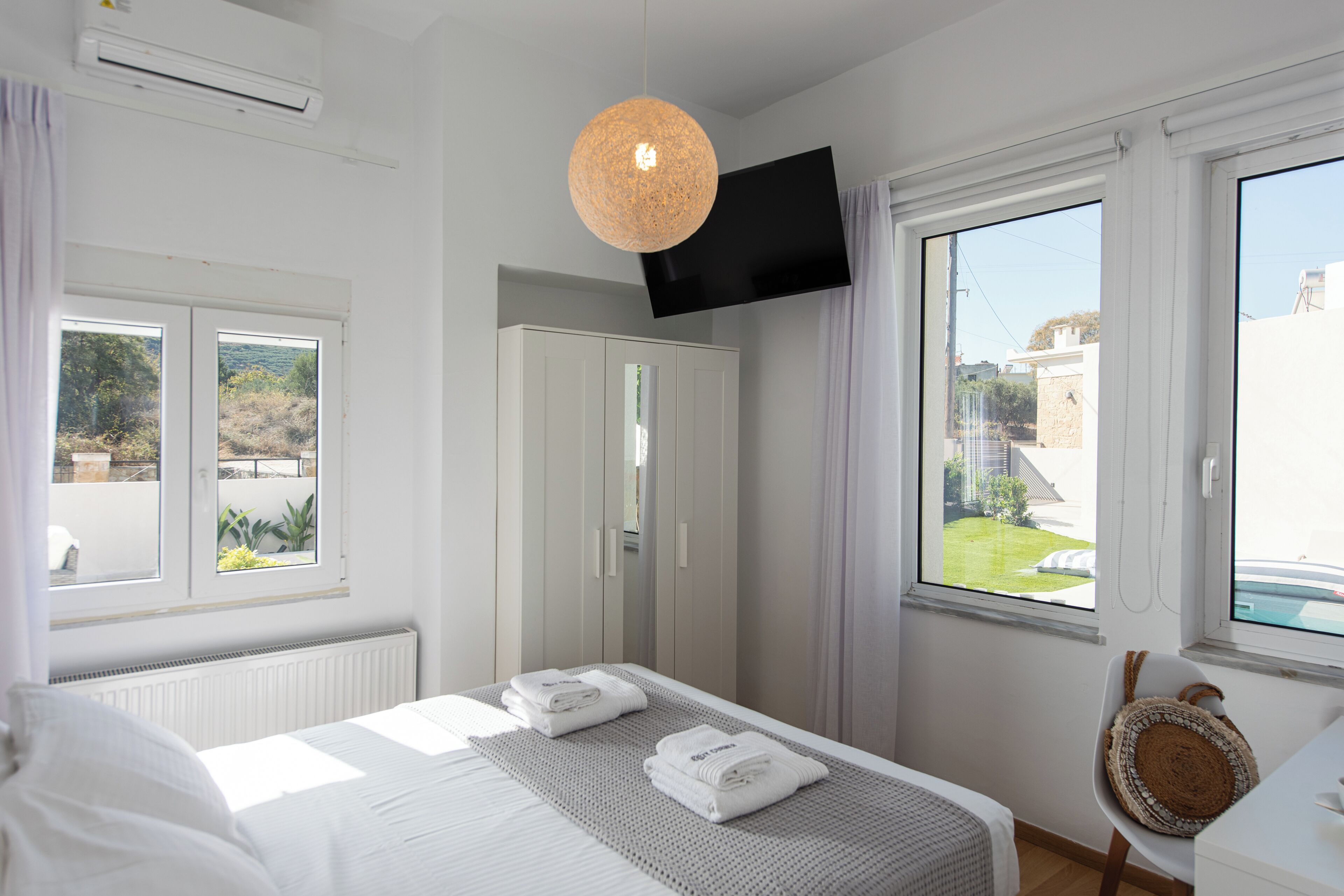 Un dormitorio con cama, armario, televisor montado en la pared y ventana con vistas al exterior.