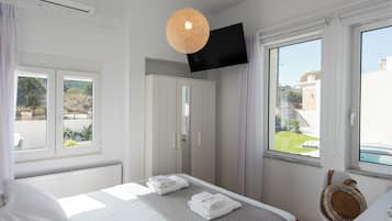 Un dormitorio con cama, armario, televisor montado en la pared y ventana con vistas al exterior.