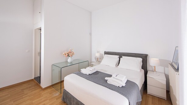 A modern hotel room with a large bed, bedside tables, a glass partition, and a ceiling fan. - Azure West by Cozy Corner (Ag. Georgios)