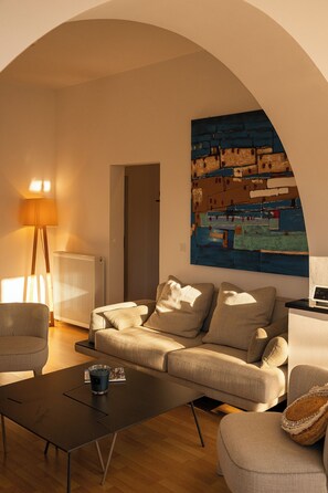 Een woonkamer met een bank, een salontafel, een lamp en een schilderij aan de muur.