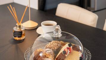 Una mesa de comedor con una campana de cristal sobre un postre, una taza de café y una botella de perfume.