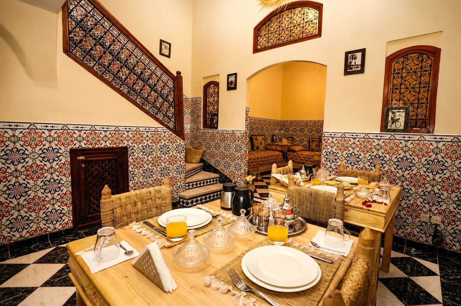 Un comedor con piso a cuadros, una escalera con barandillas ornamentadas y una habitación con paredes estampadas.