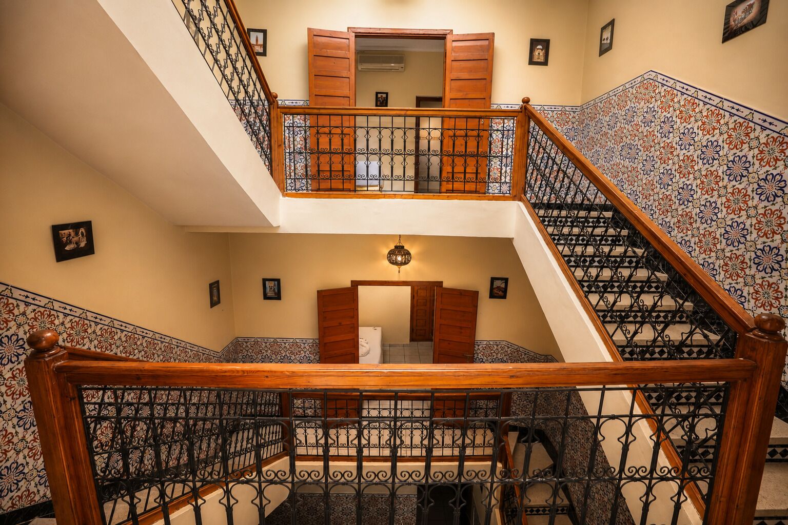 Un intérieur à plusieurs niveaux, agrémenté d’un escalier en bois, de rampes en métal décorées et de carreaux muraux à motifs.
