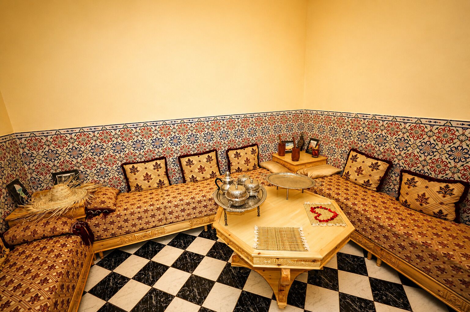 A corner room with a checkered floor, a sofa with patterned cushions, a small table with a tray, and a decorative wall.