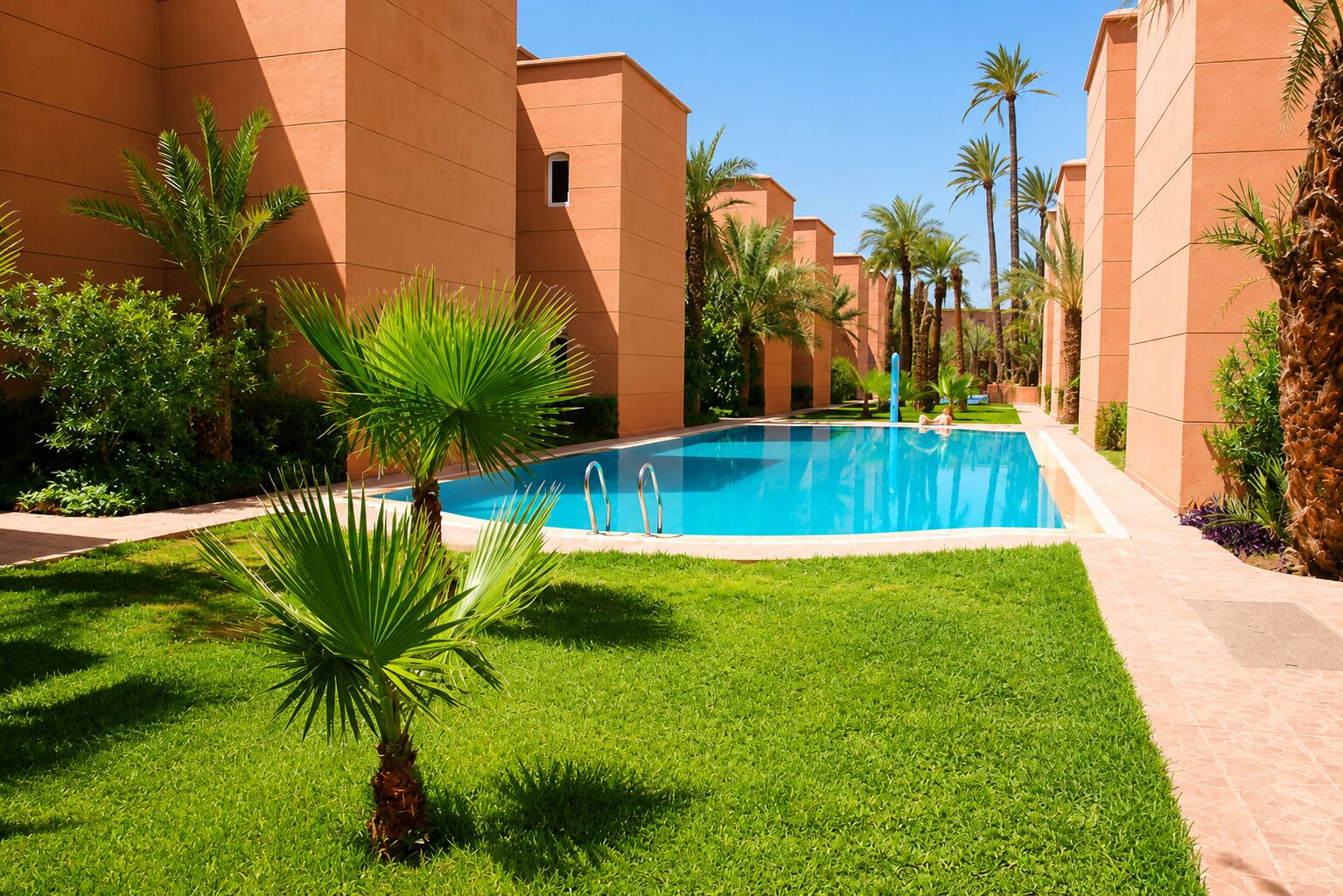 A swimming pool surrounded by palm trees and greenery, with buildings in the background.