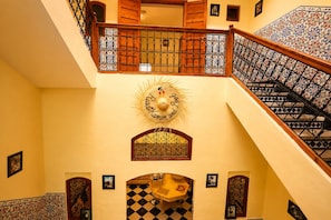 Un interior de varios niveles con una escalera, detalles decorativos en las paredes y baldosas estampadas.