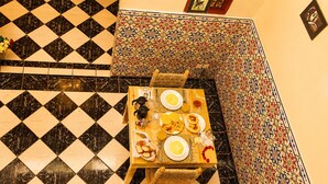 A dining table with plates, glasses, and a woven basket, set on a black and white checkered floor with a patterned wall in the background. - Riad Kamin And Pool (Marrakech)