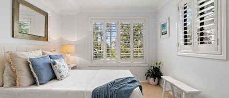 A bedroom with a bed, bedside table, lamp, window with shutters, and a bench.