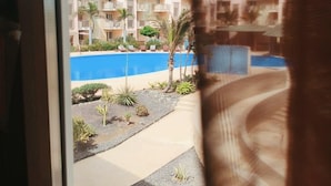 A view of a hotel pool area with a clear sky, palm trees, and a building with balconies. - HostySpot - Tropical Resort, 1-Bedroom Apartment (Santa Maria)