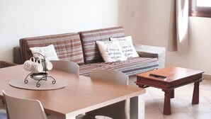 A living room with a sofa, a coffee table, and a dining table with chairs. - HostySpot - Tropical Resort, 1-Bedroom Apartment (Santa Maria)