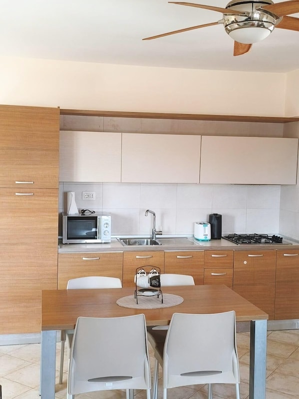 A modern kitchen with a dining table, chairs, a ceiling fan, a microwave, a toaster, and a gas stove.