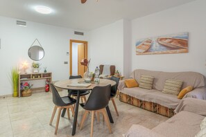 A living room with a sofa, a dining table with chairs, a coffee table, a painting on the wall, and a door leading to another room. - Aguilas Center & Costa, with Balcony, Wi-Fi and Air Conditioning (Aguilas)