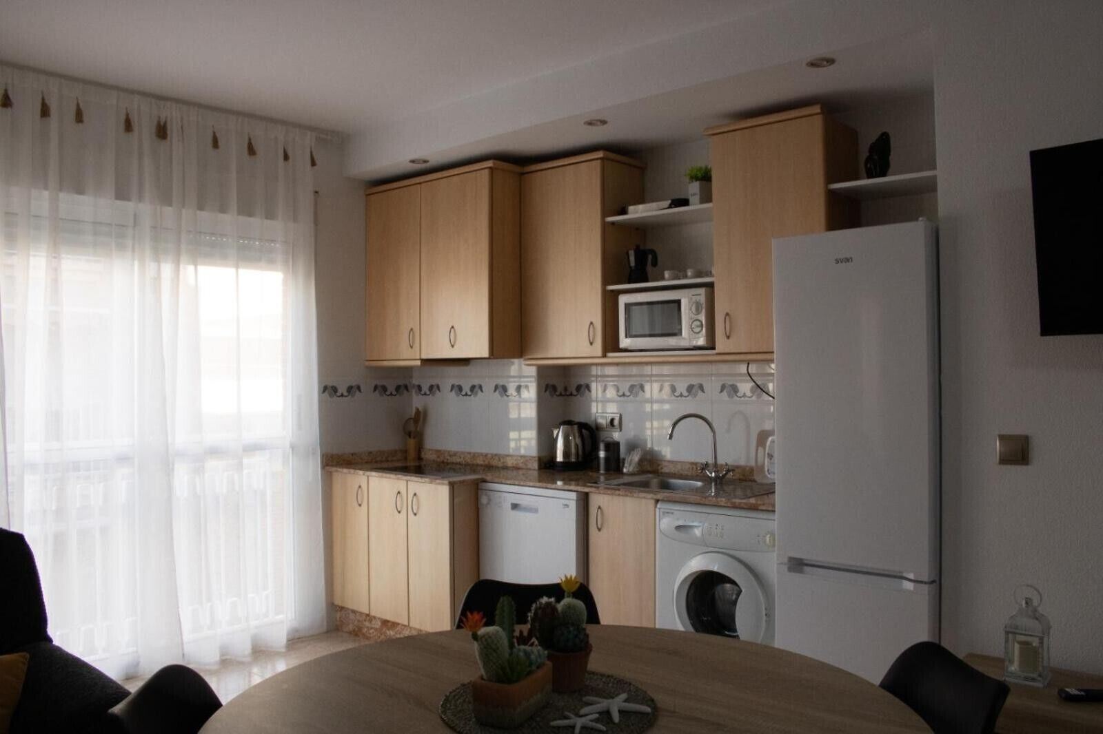 Una cocina moderna con armarios de madera, microondas, fregadero, lavavajillas y refrigerador.