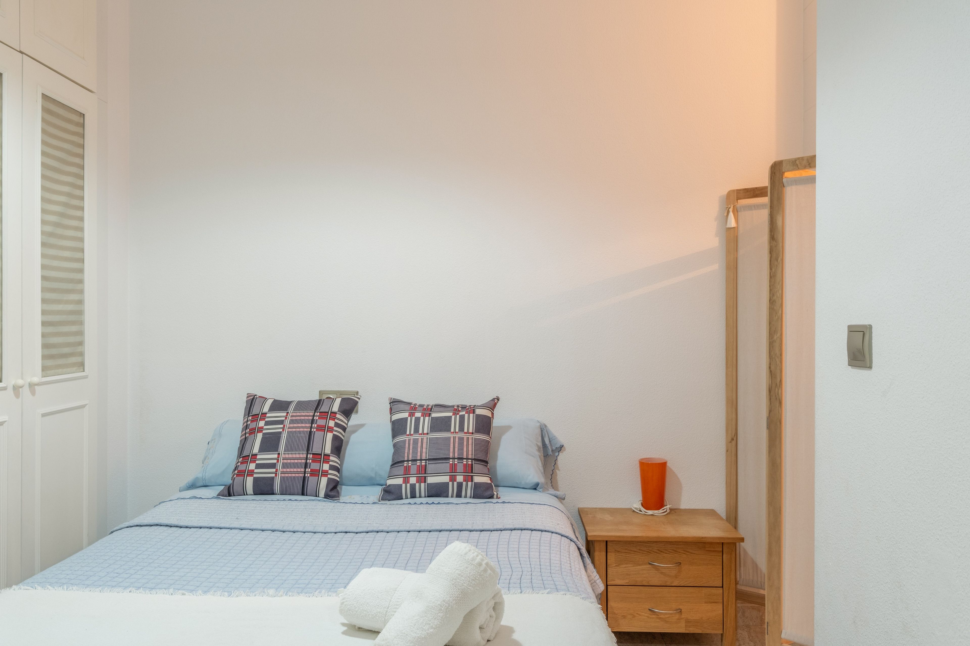 A bedroom with a bed, two pillows, a bedside table, a nightstand, and a mirror.