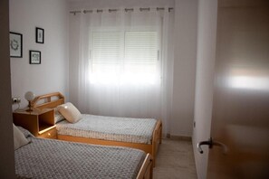 A bedroom with two single beds, a bedside table with a lamp, a window with blinds, and a door. - Aguilas Center & Costa, with Balcony, Wi-Fi and Air Conditioning (Aguilas)