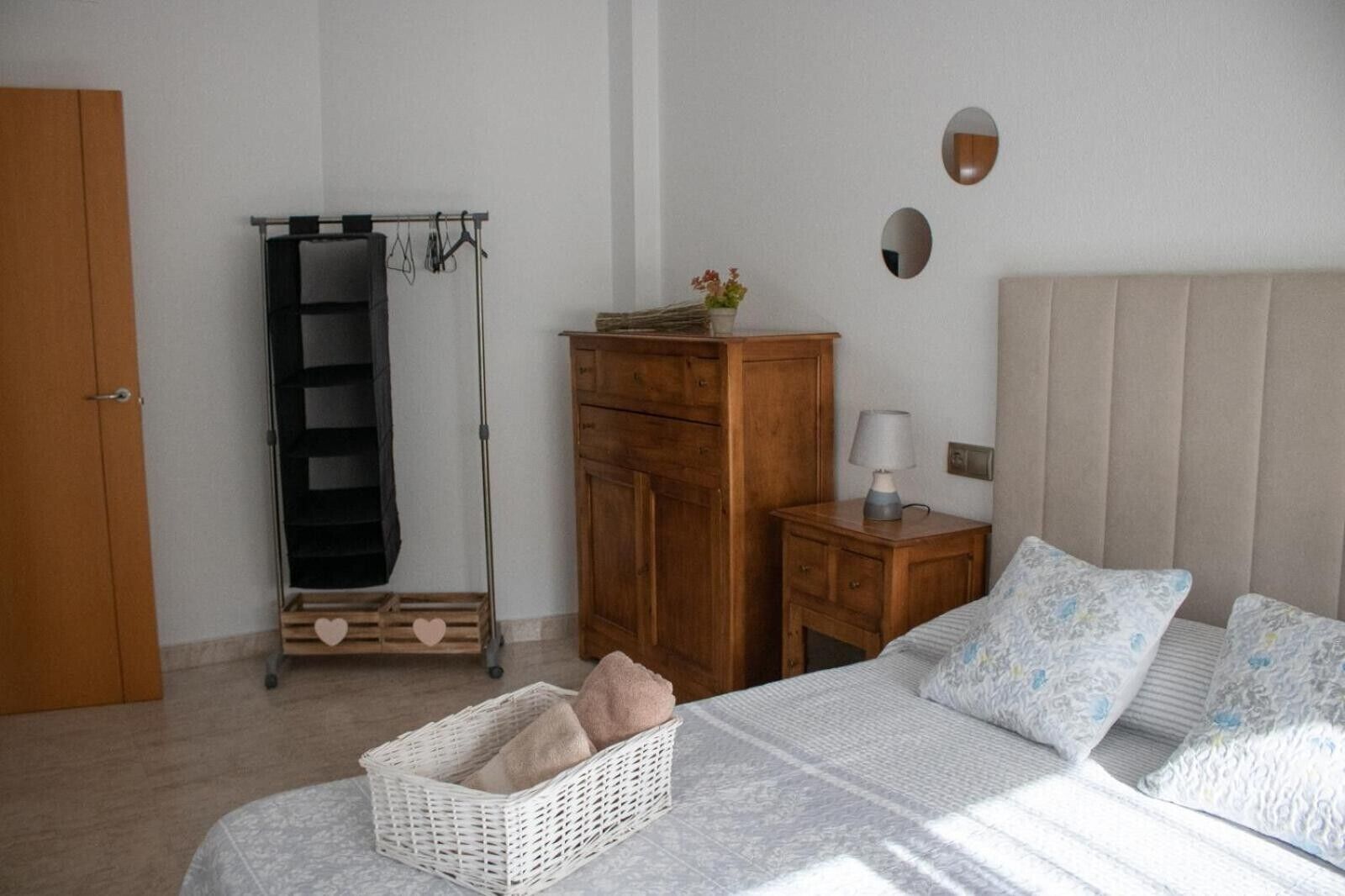 Un dormitorio con cama, mesitas de noche, armario, perchero y una planta pequeña.