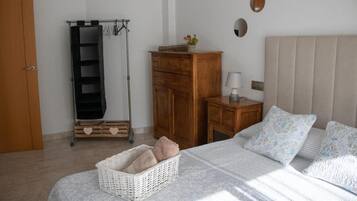 Un dormitorio con cama, mesitas de noche, armario, perchero y una planta pequeña.